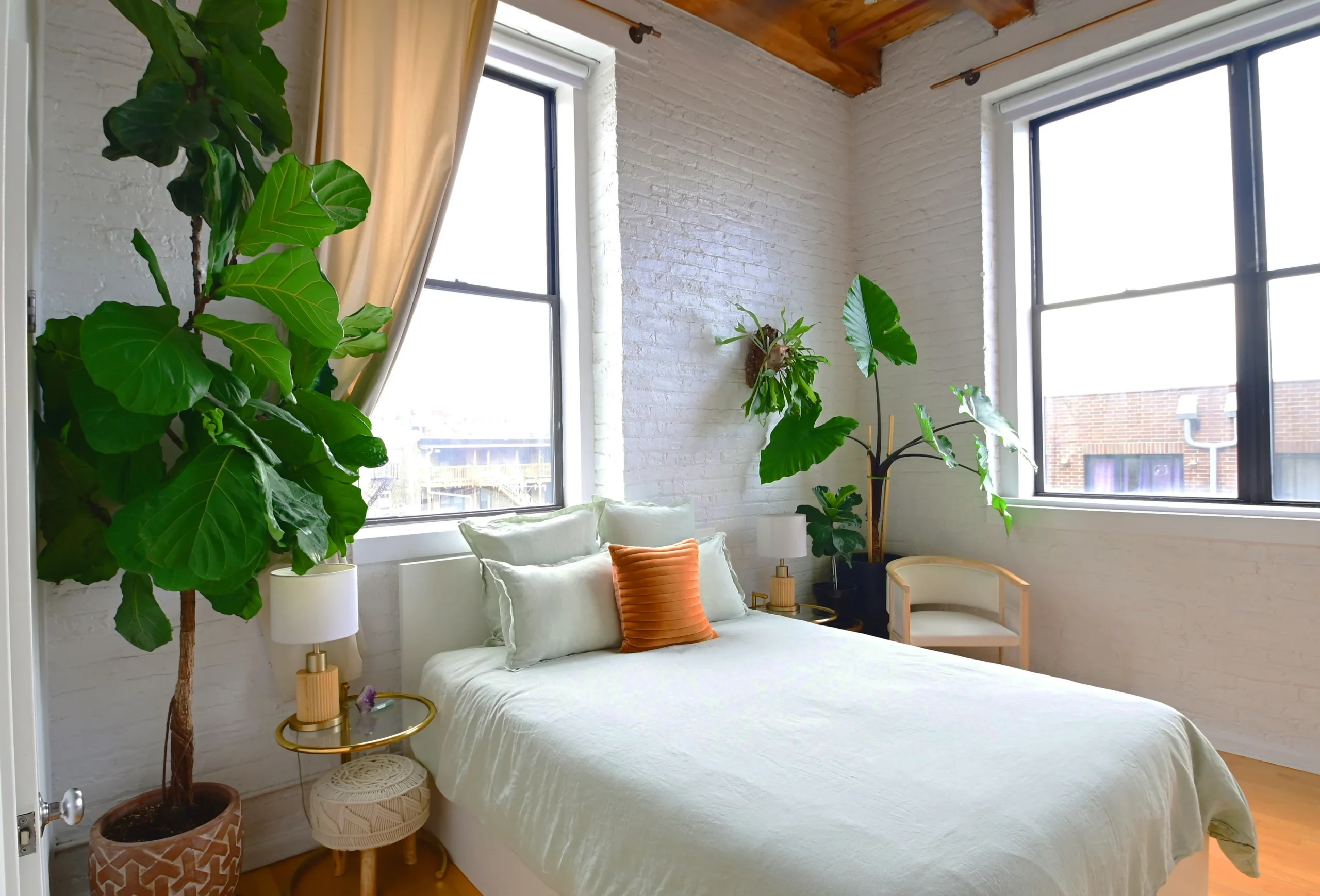 A tastefully decorated bedroom featuring a large white bed, lush green plants, and a large window with natural light streaming in. Chicago Loft project styled and designed by Laure Leger Studio